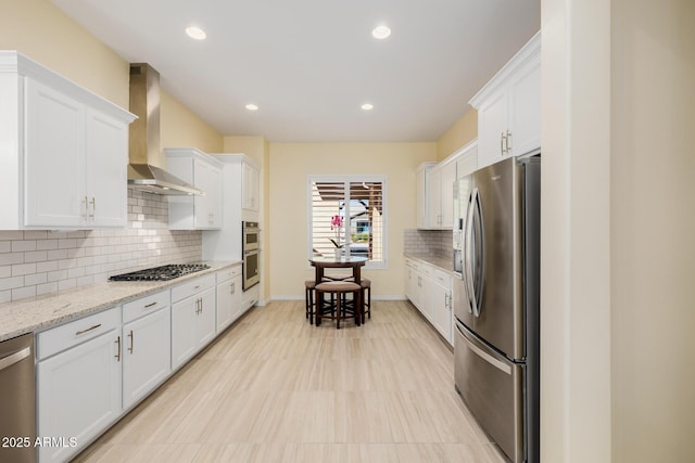 kitchen with tasteful backsplash, baseboards, wall chimney range hood, white cabinetry, and stainless steel appliances