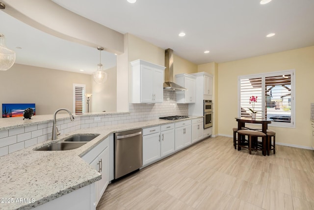 kitchen with tasteful backsplash, white cabinets, wall chimney exhaust hood, a sink, and appliances with stainless steel finishes