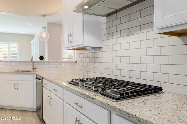 kitchen with tasteful backsplash, white cabinetry, stainless steel gas stovetop, a sink, and ventilation hood