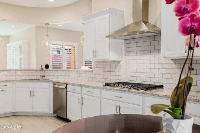 kitchen featuring a sink, wall chimney range hood, white cabinetry, decorative backsplash, and stainless steel gas cooktop