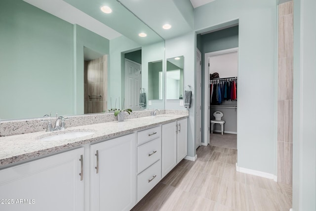full bathroom with double vanity, a sink, a spacious closet, and baseboards