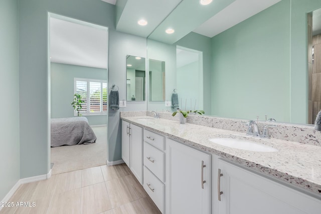 ensuite bathroom featuring double vanity, a sink, ensuite bathroom, and baseboards