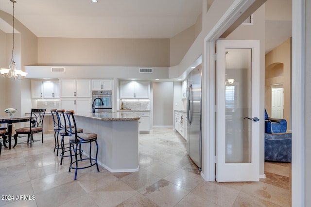 kitchen with a high ceiling, white cabinets, decorative light fixtures, light stone counters, and stainless steel appliances