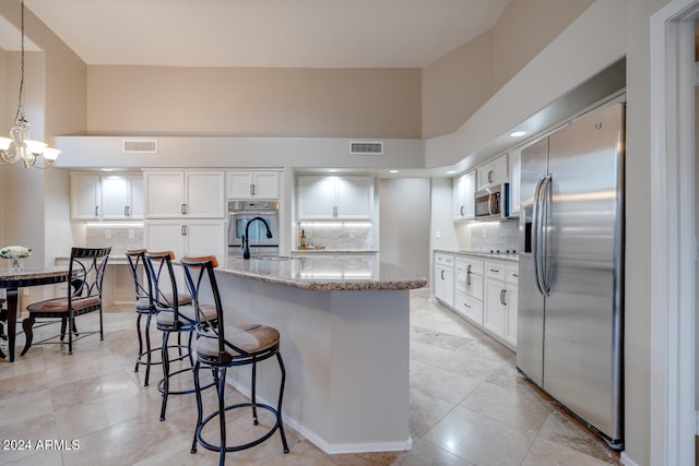 kitchen with tasteful backsplash, light stone counters, stainless steel appliances, white cabinets, and hanging light fixtures