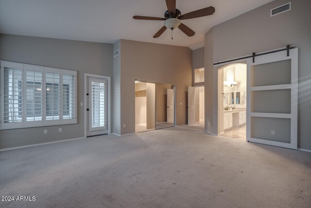 unfurnished living room with a barn door, light colored carpet, built in features, and ceiling fan