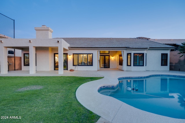 pool at dusk featuring a lawn and a patio area