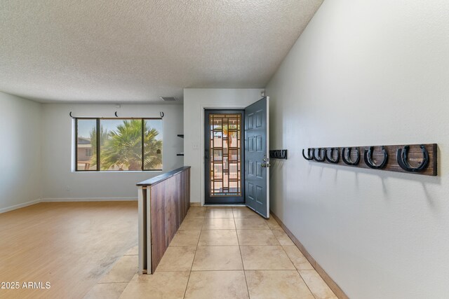 foyer entrance featuring a textured ceiling, baseboards, and light tile patterned flooring