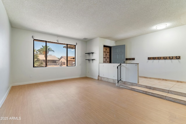 empty room with light wood-style flooring, a textured ceiling, and baseboards