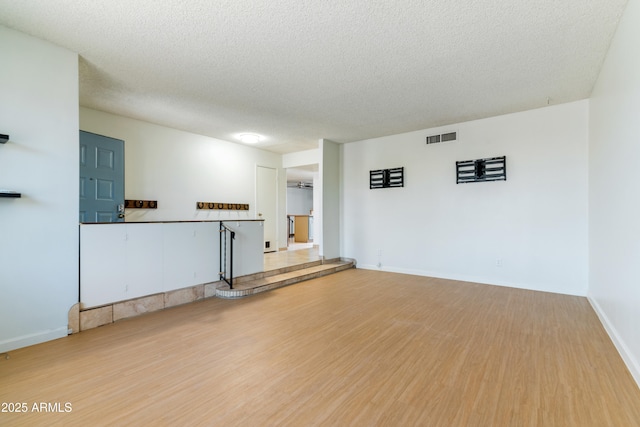 unfurnished living room featuring light wood-style floors, a textured ceiling, and baseboards