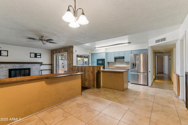 kitchen with stainless steel refrigerator with ice dispenser, a peninsula, a textured ceiling, a brick fireplace, and black microwave