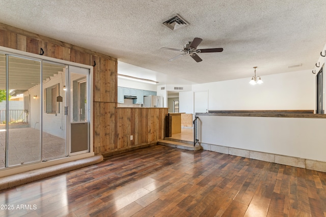 spare room with ceiling fan, dark wood finished floors, wood walls, a textured ceiling, and a chandelier
