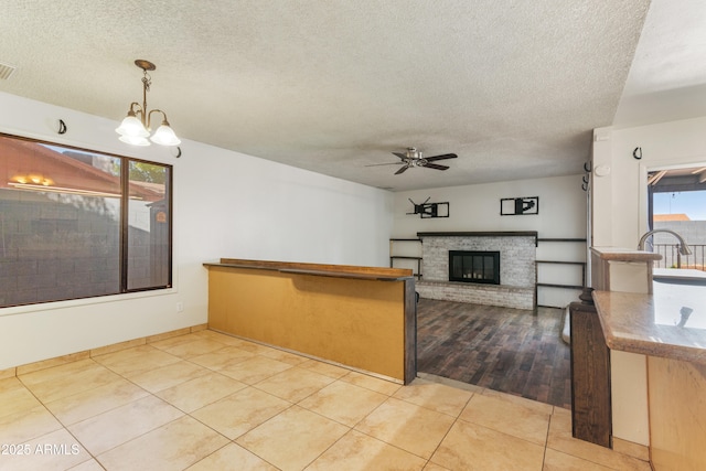 kitchen with a textured ceiling, ceiling fan, a fireplace, pendant lighting, and a chandelier