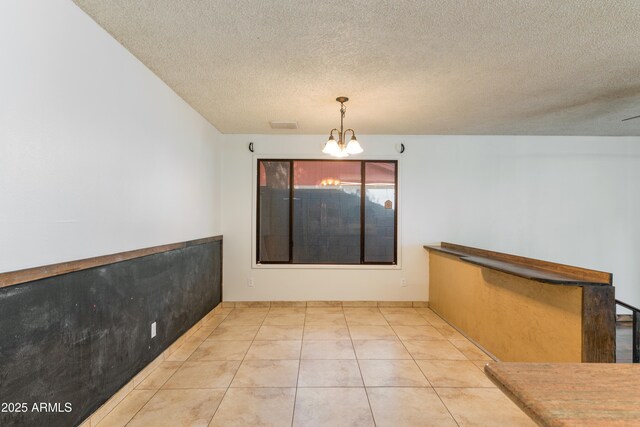 unfurnished dining area featuring a chandelier, a textured ceiling, and tile patterned flooring