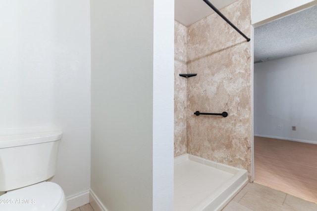 bathroom with tile patterned floors, toilet, a tile shower, and baseboards