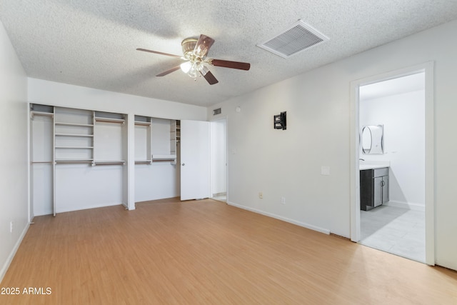 unfurnished bedroom with two closets, light wood-style floors, a textured ceiling, connected bathroom, and ceiling fan