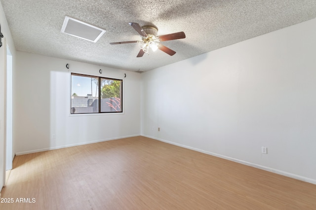 unfurnished room with a textured ceiling, light wood-style flooring, a ceiling fan, attic access, and baseboards