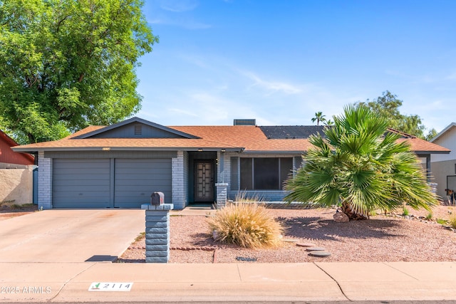 single story home featuring an attached garage, solar panels, driveway, brick siding, and roof with shingles