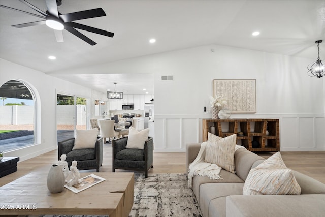 living room with lofted ceiling, light wood-style flooring, visible vents, and a decorative wall