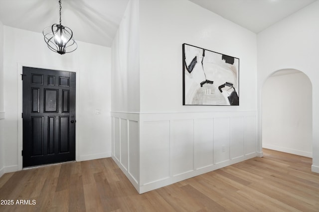 entrance foyer featuring light wood finished floors, arched walkways, a chandelier, and a decorative wall