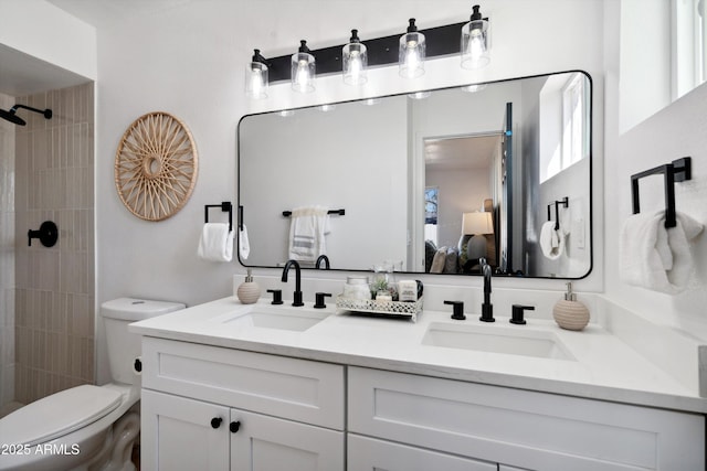 ensuite bathroom featuring toilet, double vanity, a tile shower, and a sink