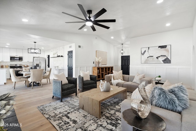 living area featuring light wood finished floors, visible vents, a wainscoted wall, vaulted ceiling, and a decorative wall