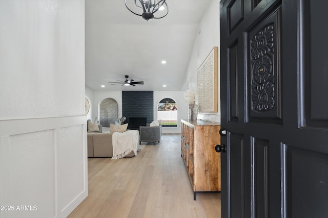 foyer entrance with ceiling fan with notable chandelier, a fireplace, light wood-style flooring, and recessed lighting