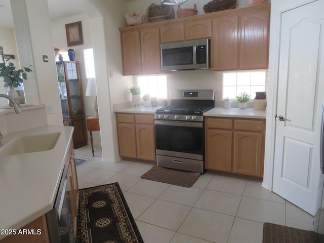kitchen with appliances with stainless steel finishes, arched walkways, a sink, light tile patterned floors, and light countertops