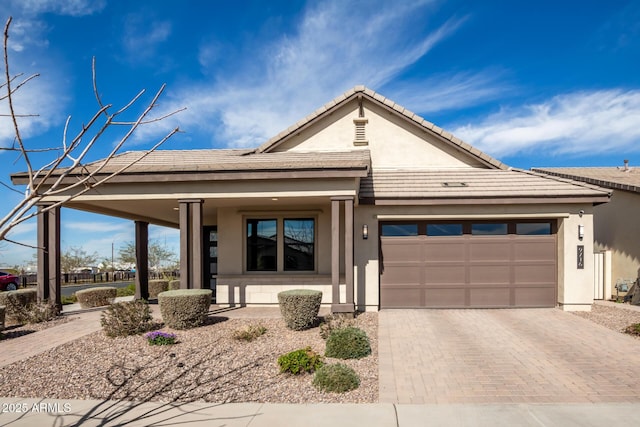 view of front facade with a garage, a tiled roof, decorative driveway, and stucco siding