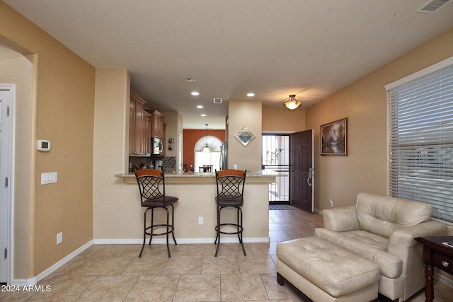 kitchen featuring hanging light fixtures, light tile patterned floors, tasteful backsplash, a kitchen bar, and kitchen peninsula