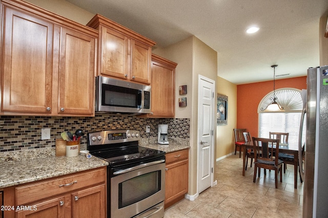 kitchen featuring hanging light fixtures, stainless steel appliances, light stone counters, decorative backsplash, and light tile patterned floors