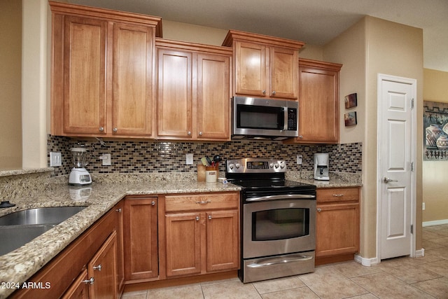 kitchen with backsplash, light stone counters, light tile patterned flooring, and stainless steel appliances