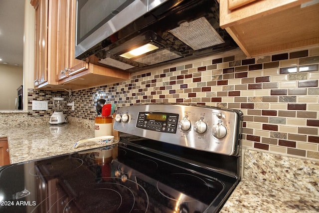 kitchen with tasteful backsplash, light stone counters, and stainless steel range oven