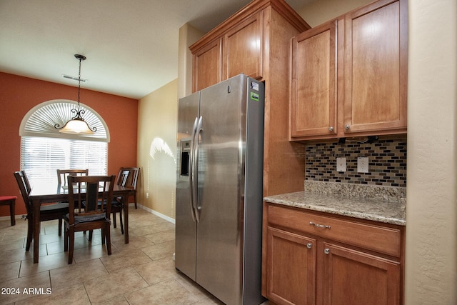 kitchen featuring decorative backsplash, light stone countertops, stainless steel refrigerator with ice dispenser, and decorative light fixtures