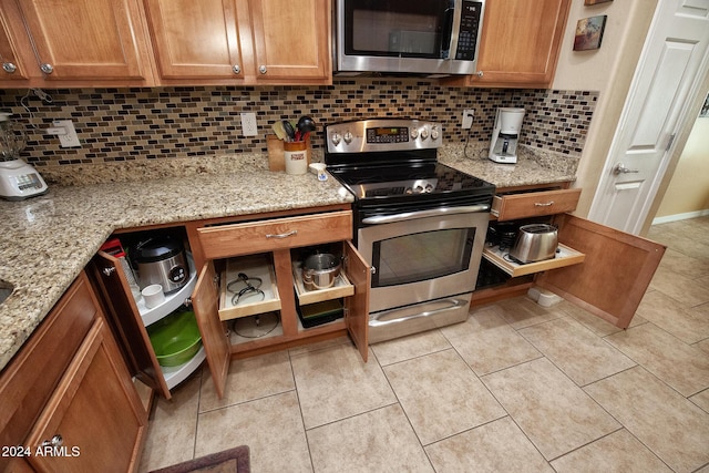 kitchen with tasteful backsplash, light stone counters, light tile patterned floors, and appliances with stainless steel finishes