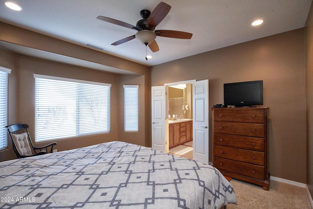 bedroom with ceiling fan, light colored carpet, and connected bathroom