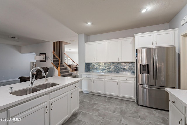 kitchen with white cabinetry, stainless steel fridge, backsplash, and sink