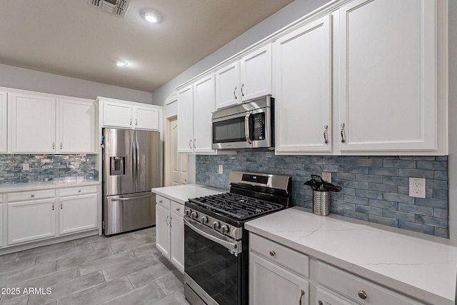 kitchen with white cabinets, appliances with stainless steel finishes, light stone countertops, and backsplash