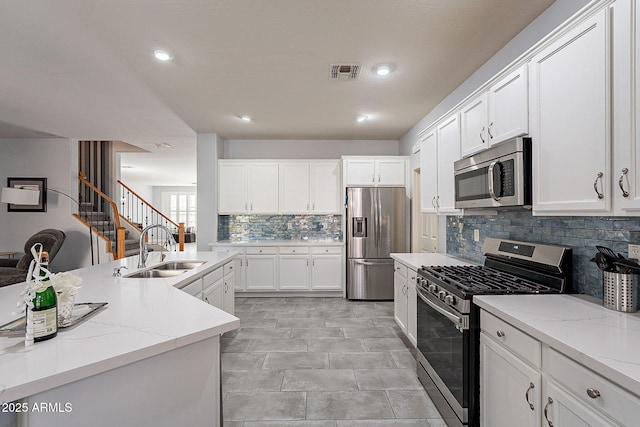 kitchen with appliances with stainless steel finishes, white cabinets, light stone countertops, and sink