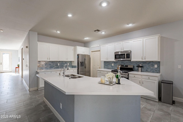 kitchen featuring appliances with stainless steel finishes, white cabinets, a center island with sink, and sink