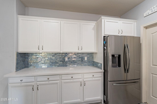 kitchen featuring white cabinetry, backsplash, light stone counters, and stainless steel fridge