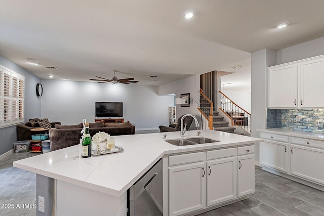 kitchen with sink, white cabinets, stainless steel dishwasher, and a center island with sink