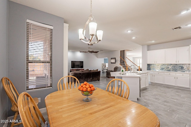 dining space featuring sink, light wood-type flooring, and ceiling fan with notable chandelier