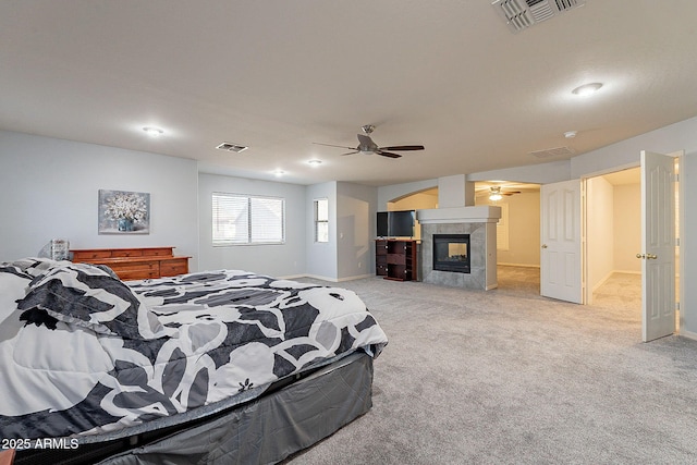 bedroom featuring a tiled fireplace, ceiling fan, and light carpet