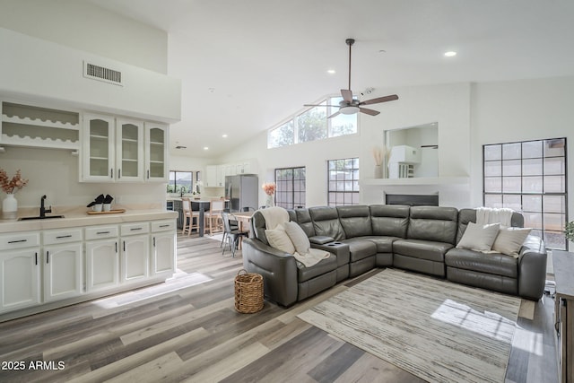 living room with light wood-type flooring, high vaulted ceiling, ceiling fan, and sink