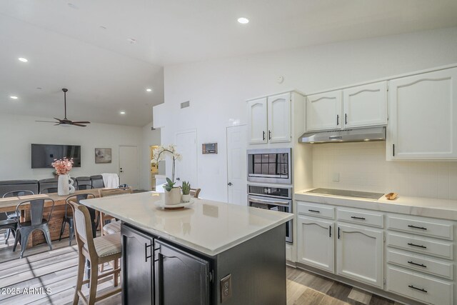 kitchen with white cabinets, decorative backsplash, stainless steel oven, and vaulted ceiling