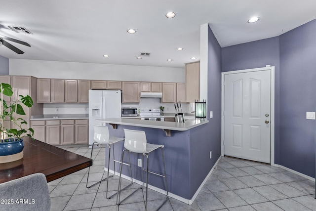 kitchen with white appliances, light brown cabinetry, kitchen peninsula, and a breakfast bar area