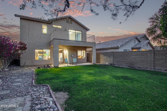 back house at dusk with a balcony, a yard, and a patio area