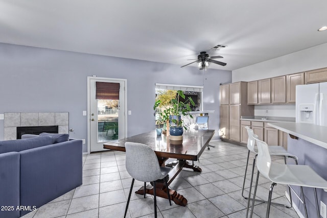 dining area featuring a tiled fireplace, ceiling fan, and light tile patterned flooring