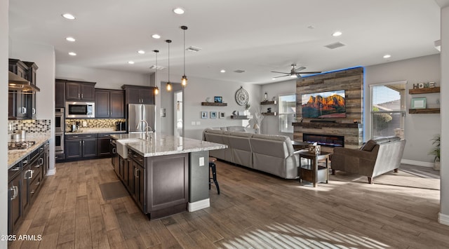 kitchen with a kitchen bar, sink, hanging light fixtures, stainless steel appliances, and a kitchen island with sink