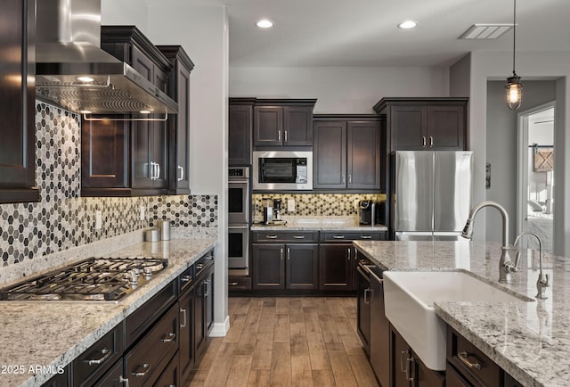 kitchen featuring dark brown cabinetry, appliances with stainless steel finishes, sink, and wall chimney range hood